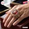 Closeup of Brisbane Lions 2026 Three-Peat Gold Ring worn on a hand over a wooden box.