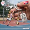 Close-up of a Caitlin Clark USA Basketball 2026 World Cup keychain held in a hand over a court background.