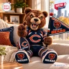 Front view of a brown bear mascot stuffed toy wearing a team jersey, holding a football and a flag on a sofa.