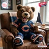 Front view of a plush mascot pillow wearing a blue football jersey holding a small flag while sitting in a leather armchair.