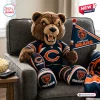 Front view of a brown plush bear mascot pillow wearing a blue and orange jersey while sitting in an armchair.