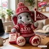 Front view of a crochet elephant plush doll wearing a red hat and sweater with Greek letters and holding a matching flag.
