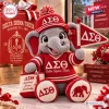 Front view of a crochet elephant plush doll wearing a red jersey and cap with Greek letters and holding a felt flag.