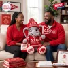 A couple sits on a couch holding a Delta Sigma Theta crochet elephant plush doll wearing a red hat and jersey.