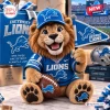 Front view of a crocheted lion mascot plush holding a football and a pennant flag in Detroit Lions gear.