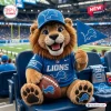 Front view of a plush lion wearing a team jersey and hat while holding a pennant and football in a stadium.