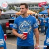 Front view of a man wearing a blue T-shirt with Stay In Your Lane text and a lion graphic in a stadium parking lot.