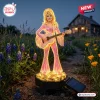 Front view of Dolly Parton Limited Edition Solar Garden Light glowing in a garden setting at dusk.