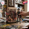 Hand holding a Dr. Frank-N-Furter 50th Anniversary Hot Toys figure next to its display box on a wooden desk.