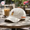 Side angle of a beige baseball cap with an embroidered coffee cup graphic and orange Dunkin Donuts branding.