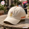 Side view of a beige baseball cap featuring a coffee cup embroidery with a logo, resting on a wooden table.