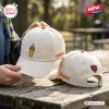Close-up view of two off-white baseball caps featuring embroidered coffee and team logo designs on a rustic table.