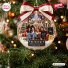 Front view of a clear circular Christmas ornament featuring a group scene and red and cream bow hanging on a tree.