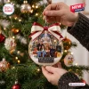 Hand holding a clear spherical Christmas ornament featuring a fountain and group scene with a festive ribbon on a tree.