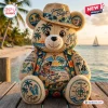 Front view of a Jimmy Buffett Plush Teddy Bear wearing a straw hat and tropical shirt sitting on a wooden dock.