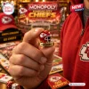Close-up of a hand holding a miniature Kansas City Chiefs football helmet token from a board game.