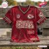 Front view of a distressed red V-neck T-shirt with football-themed Kansas City Chiefs graphics on a wooden bench.