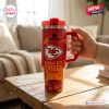 Hand holding a Kansas City Chiefs red 40 oz Stanley tumbler on a wooden table.