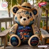 Front view of a plush bear wearing a straw hat with music and beach-themed prints in a wooden chair setting.