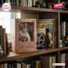 Marilyn Monroe 100th Anniversary Hot Toys Figure inside a gold-trimmed display box on a wooden bookshelf.