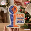 Close-up of a hand holding a New York Knicks 2026 NBA Champions acrylic ornament with a basketball and trophy graphic.