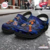 Pair of blue camo clogs with basketball team charms sitting on an asphalt street.