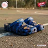 Side view of New York Knicks blue camo clogs with charms resting on outdoor pavement.