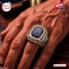 Close-up of a hand wearing a Notre Dame Fighting Irish 139th Anniversary Ring with blue stone and gold lettering.