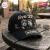 Side view of a black baseball cap featuring embroidered Oasis Live 27 text and portraits on a wooden table.