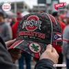 Close-up of a camo Ohio State Buckeyes baseball cap with red accents, front logo, and side Ohio state flag patch.