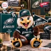 Front view of an eagle plush wearing a Philadelphia Eagles jersey and cap, holding a small team pennant and a football.