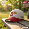 Front view of a beige and red Pokémon 30th Anniversary baseball hat resting on a wooden bench outdoors.