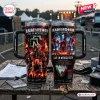 Two Stanley tumblers featuring concert photos, flames, and text on a wooden surface at an outdoor venue.