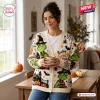 Front view of a woman wearing a cream Halloween knitted cardigan featuring green character illustrations and orange pumpkins.