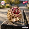 Close-up of a gold San Francisco 49ers 80th Anniversary Commemorative Ring with a large red stone on a wooden bench.