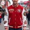 Front view of a red and white San Francisco 49ers baseball jacket with multiple patches worn outdoors.