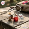 Close-up of a 75th Anniversary keychain featuring a hiker beagle figurine and a small red doghouse charm on a wood table.