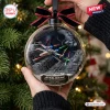 Close-up of a clear glass Christmas ornament featuring an X-wing starfighter battle scene with a black ribbon bow.