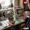 Hands holding a Star Wars Grogu in Mandalorian Armor vinyl figure and its branded display box.