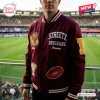 Front view of the maroon varsity jacket featuring embroidered patches and text at a stadium.