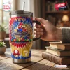 Hand holding a Stanley tumbler featuring a vibrant tie-dye pattern, anniversary text, and character graphics on a wooden table.