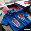 Top view of a blue polo shirt featuring a graphic print of a red and gold emblem with a ripped effect.