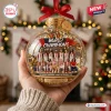 Hand holding a clear glass ornament featuring a team photo and World Champions text with a red ribbon and gold confetti.