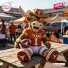 Front view of a Texas Longhorns Mascot Plush Pillow sitting on a wooden picnic table holding a football.