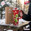 Hand holding a red 40oz Stanley tumbler with Grinch Christmas art on a snowy outdoor wooden picnic table.