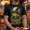 Front view of a black t-shirt featuring a green character wearing a witch hat in a moonlit Halloween graveyard scene.