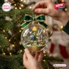 Hand holding a clear glass bauble containing a fantasy warrior scene with a green bow on a decorated Christmas tree.