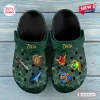 Top-down view of green clogs featuring Ocarina of Time themed charms and golden logo prints.