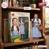 The Wizard of Oz 87th Anniversary Figure of Dorothy holding Toto next to a windowed display box on a wooden bookshelf.