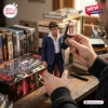 Hands holding a Tony Montana collectible figure in a blue suit with an assault rifle, displayed near movie cases.